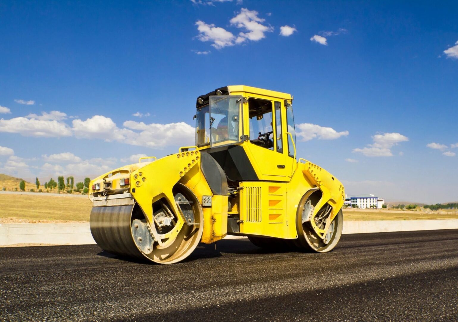 A yellow road roller is on the side of a street.